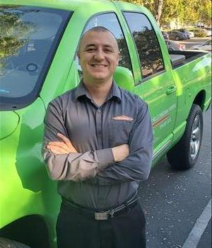 photo of male employee leaning against a green SERVPRO truck  and smiling